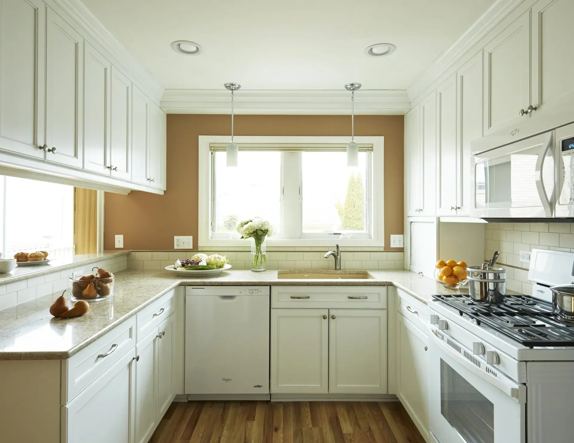 Bright white kitchen with wood floor, marble counters, gas range, and a window over the sink in Buffalo Grove, IL
