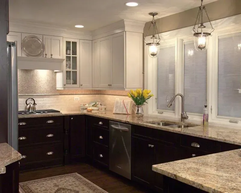 Modern kitchen with white cabinets, dark lower cabinets, granite counters, and pendant lights over the island. in a modern kitchen with gray cabinets, an island, pendant lights, exposed wood beams, and two barstools in Arlington Heights, IL.