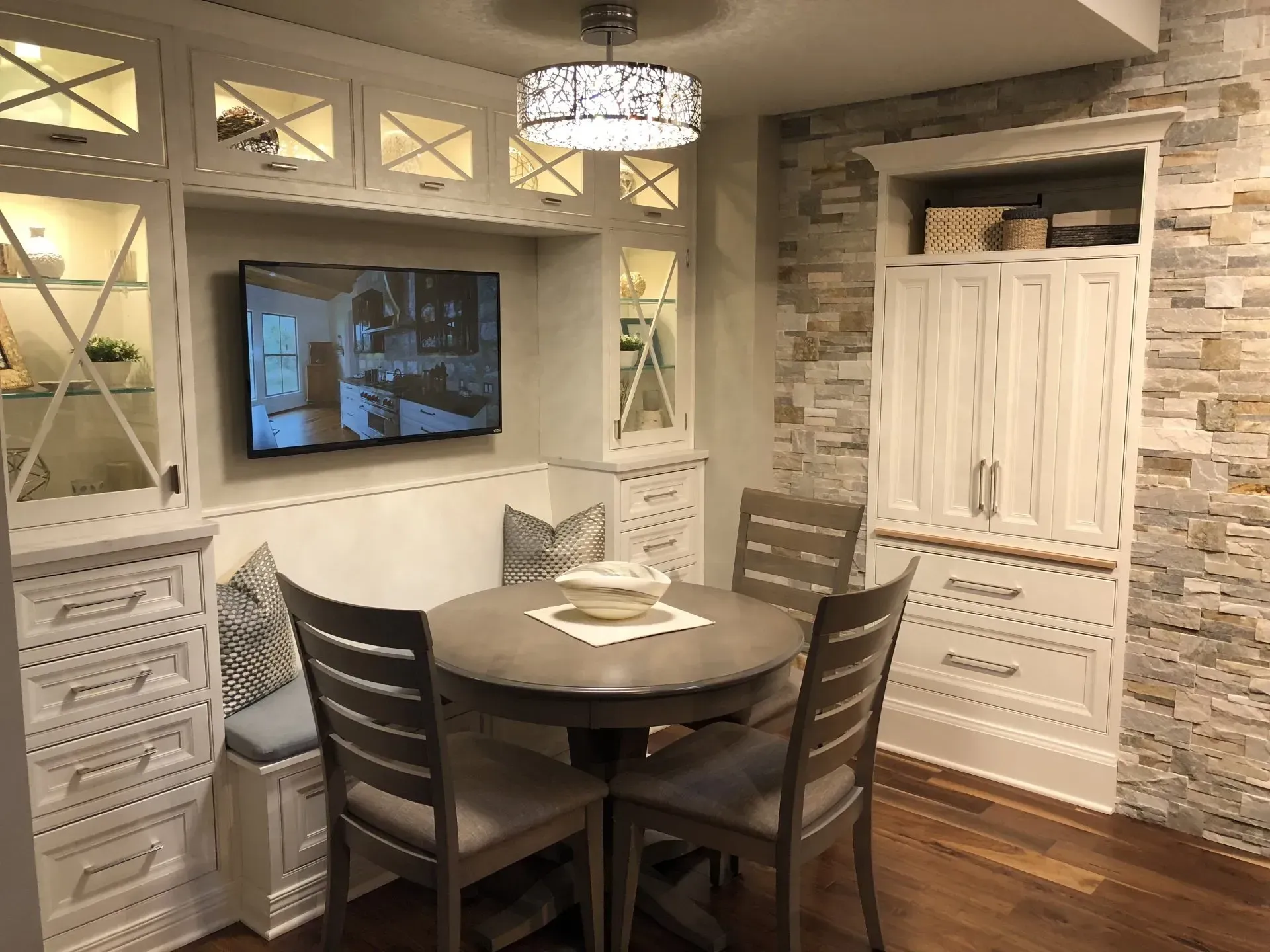 Cozy dining nook with round table, four chairs, wall TV, built-in cabinets, and wood flooring in Modern kitchen with gray cabinets, island, pendant lights, exposed wood beams, and two barstools in Arlington Heights, IL.