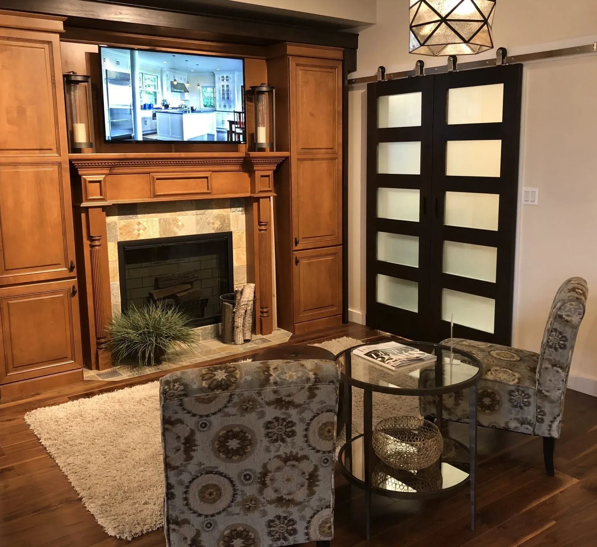 Cozy living room with wood fireplace, wall-mounted TV, and two patterned chairs around a round glass table in Modern kitchen with gray cabinets, island, pendant lights, exposed wood beams, and two barstools in Arlington Heights, IL.