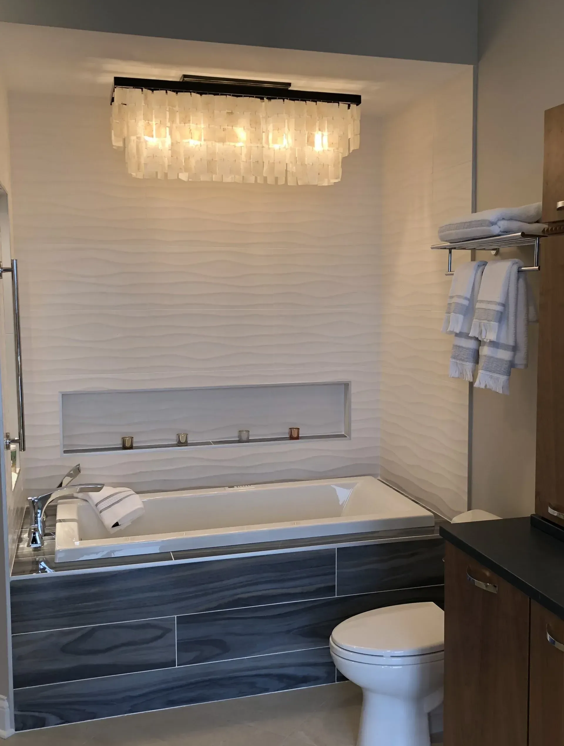 Modern bathroom with a white bathtub, toilet, dark vanity, and frosted light fixture above the tub. Modern kitchen with gray cabinets, island, pendant lights, exposed wood beams, and two barstools in Arlington Heights, IL.