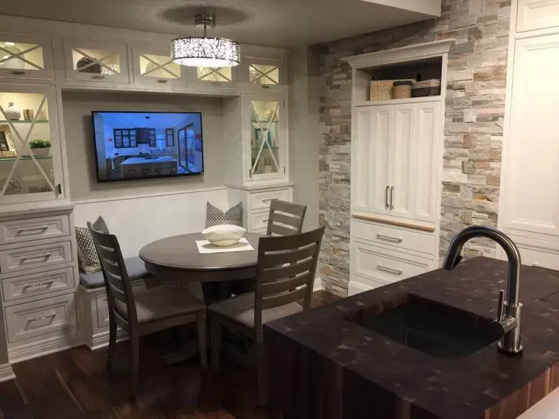 Modern kitchen with round dining table, white cabinets, wall TV, and dark island sink with faucet in Modern kitchen with gray cabinets, island, pendant lights, exposed wood beams, and two barstools in Arlington Heights, IL.
