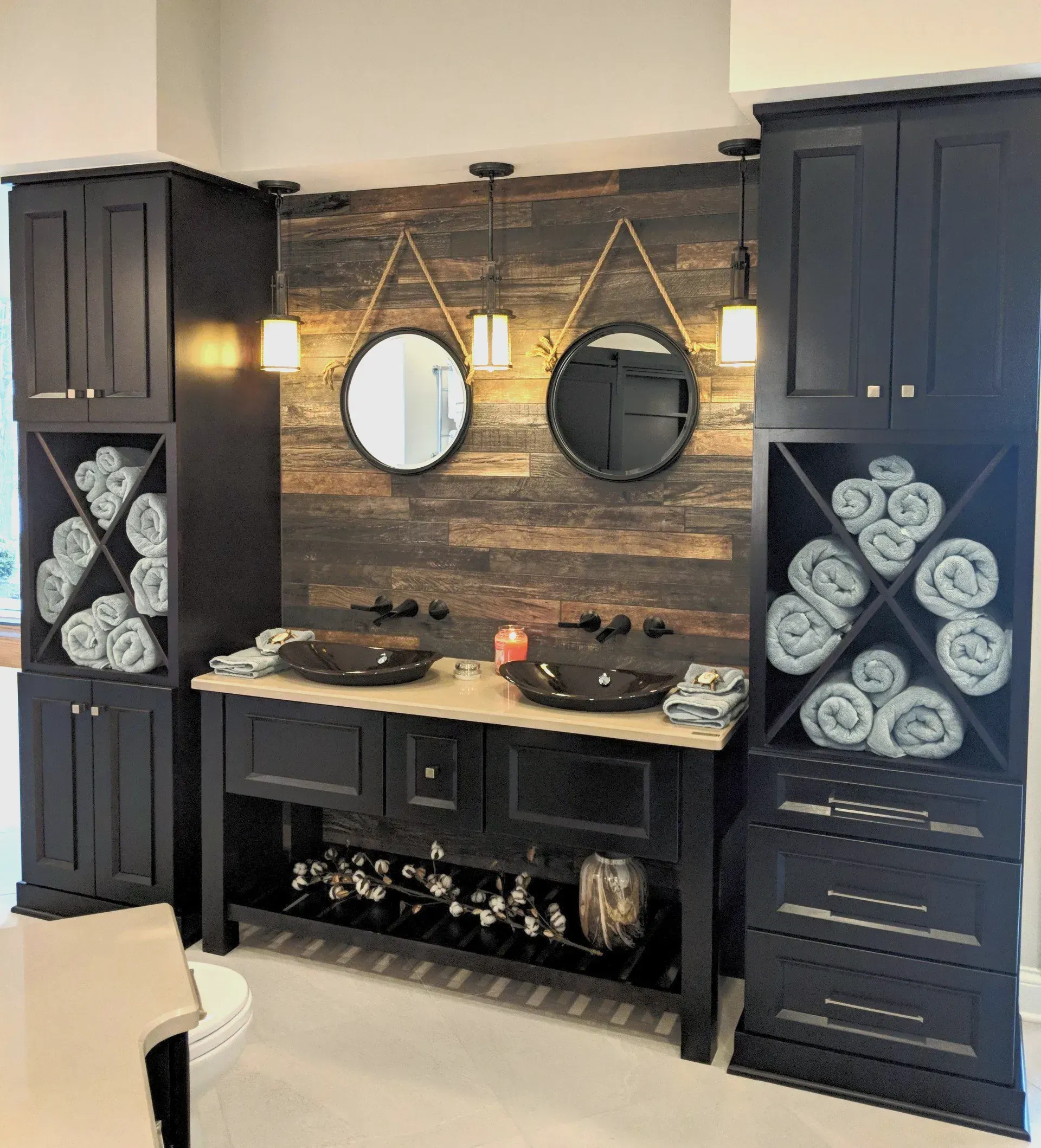 Rustic bathroom remodeling in Arlington Heights, IL, featuring a vanity with dark blue cabinets, twin round mirrors, a wood accent wall, and woven towel storage.