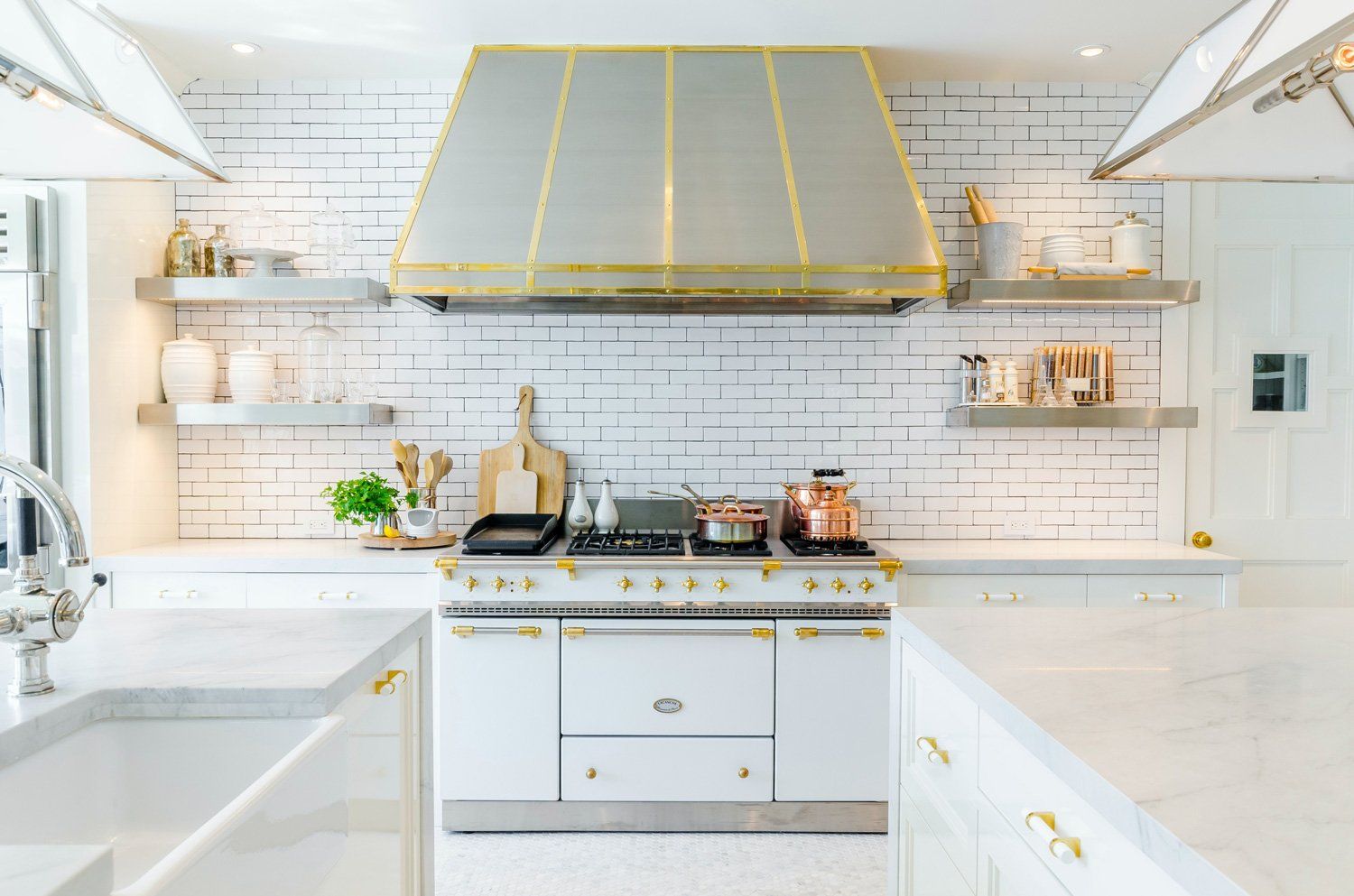 Bright white kitchen remodeling in Arlington Heights, IL, featuring gold accents, marble countertops, and a large gold range hood over the stovetop.