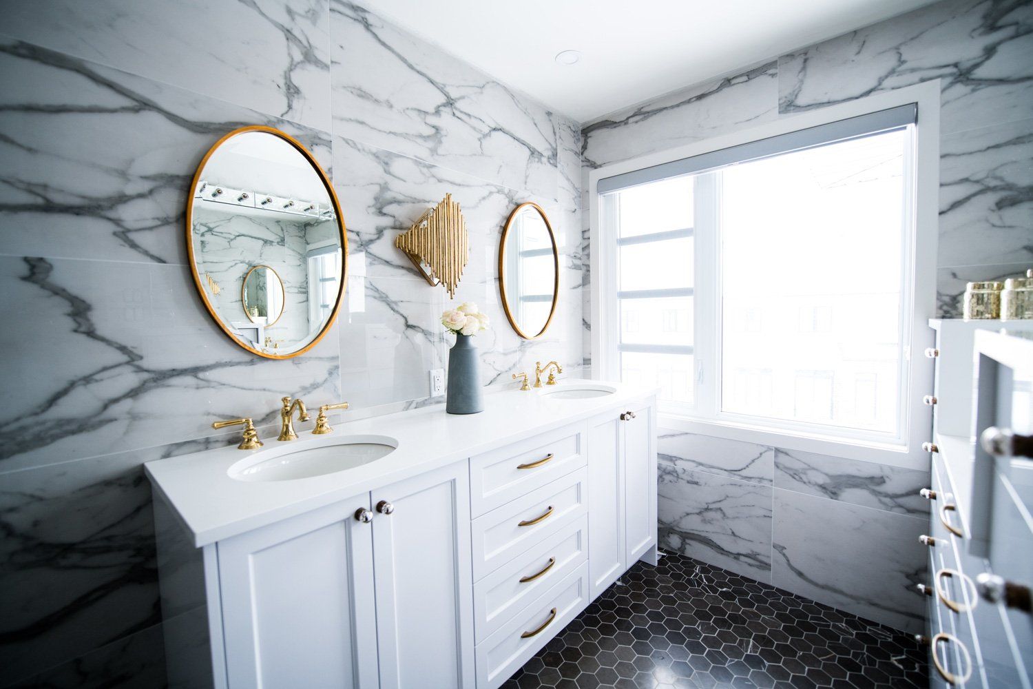 Bright marble bathroom remodeling in Arlington Heights, IL, featuring a white vanity, gold mirrors, and a large window overlooking the ocean.