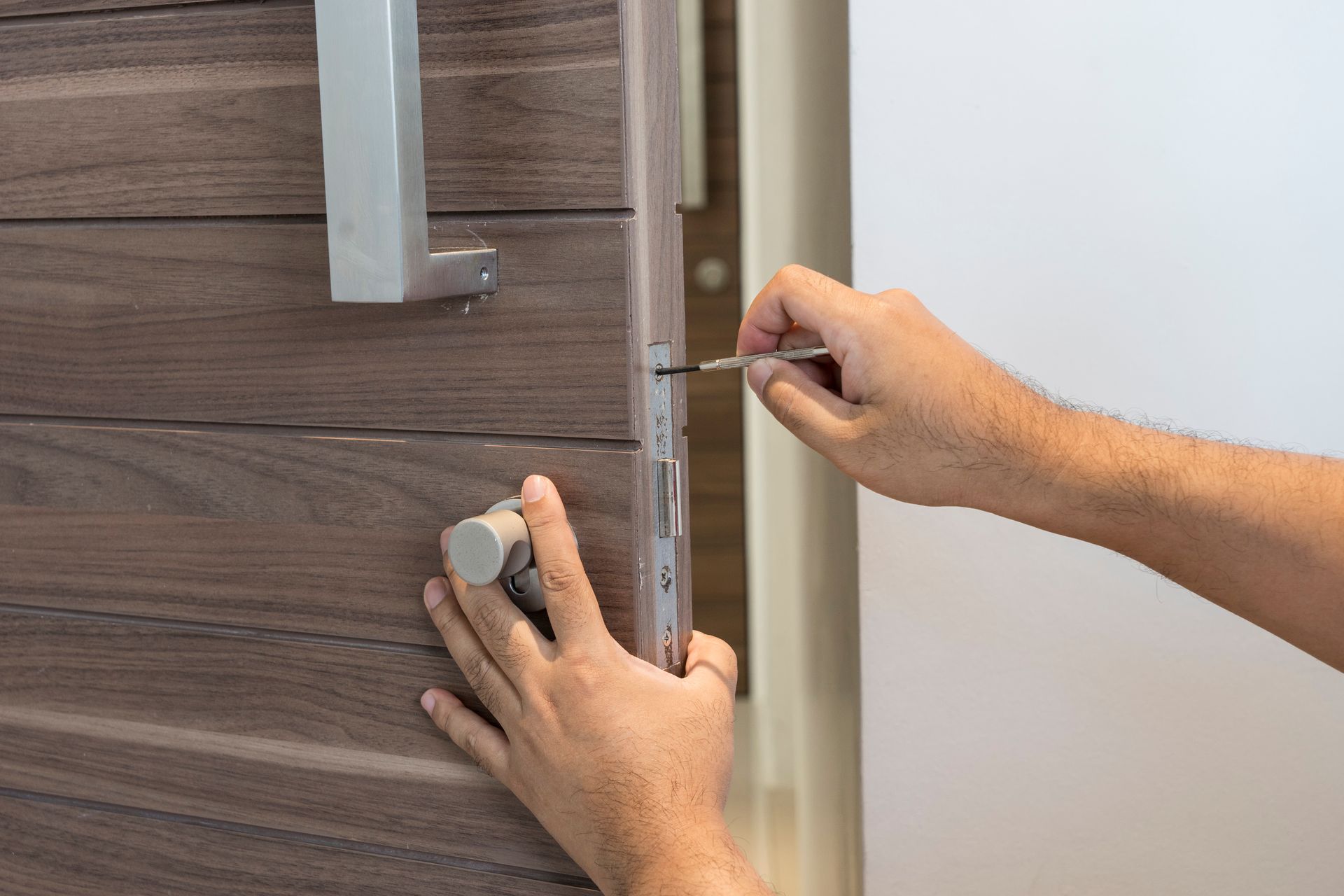 Professional commercial locksmith tightening screws on a secure building door. Professional commercial locksmith tightening screws on a secure building door.