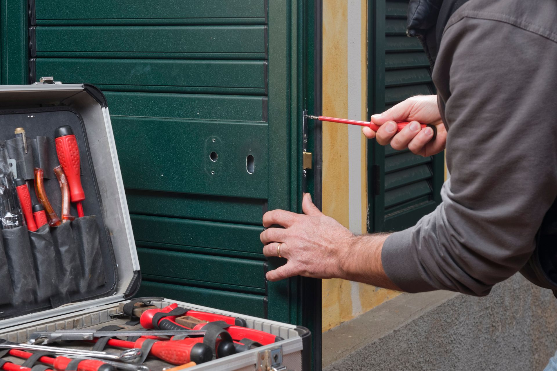 Person using a screwdriver to manipulate a lock on a green door, with a toolbox nearby.