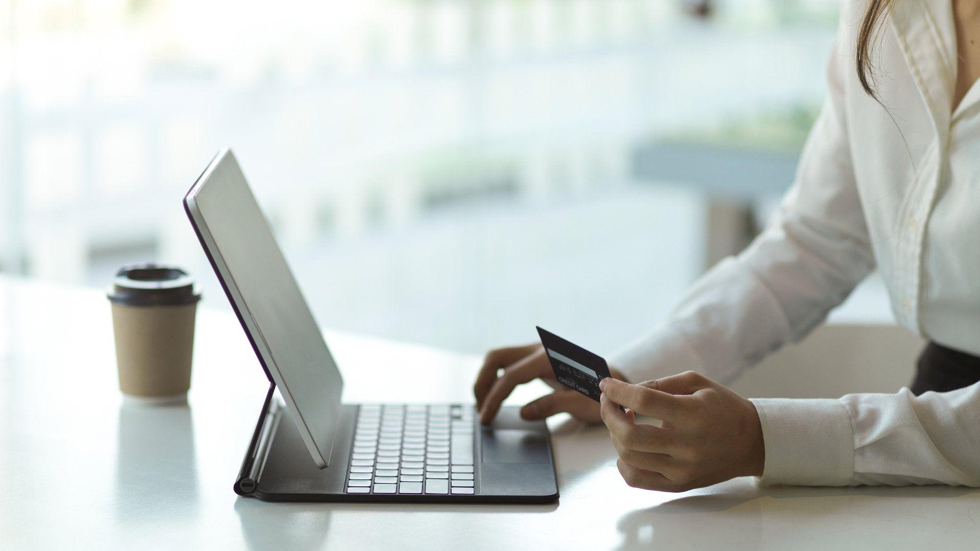 Person using a laptop and holding a credit card at a table, with a coffee cup nearby.