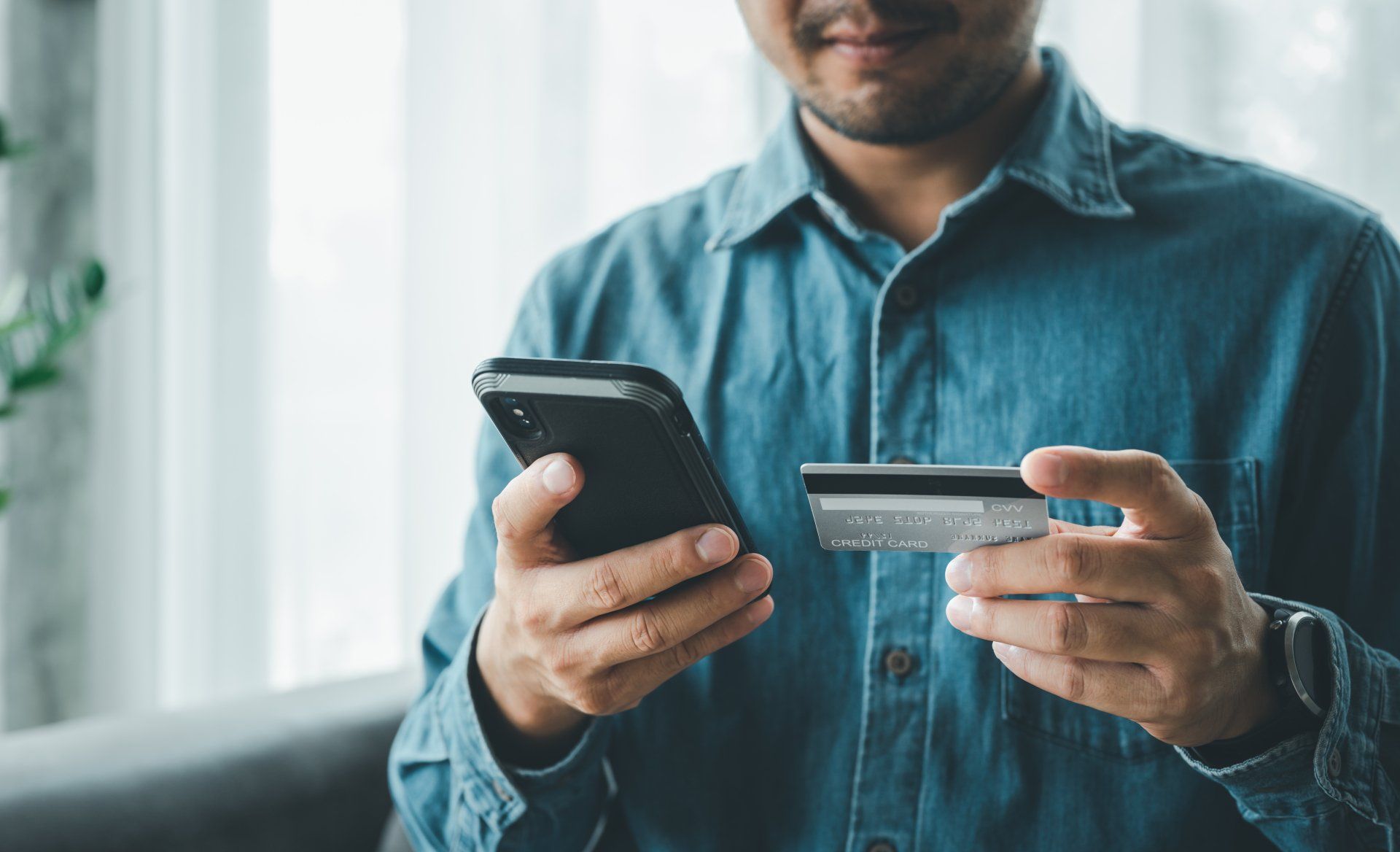Person holding a smartphone and credit card, making an online payment indoors.