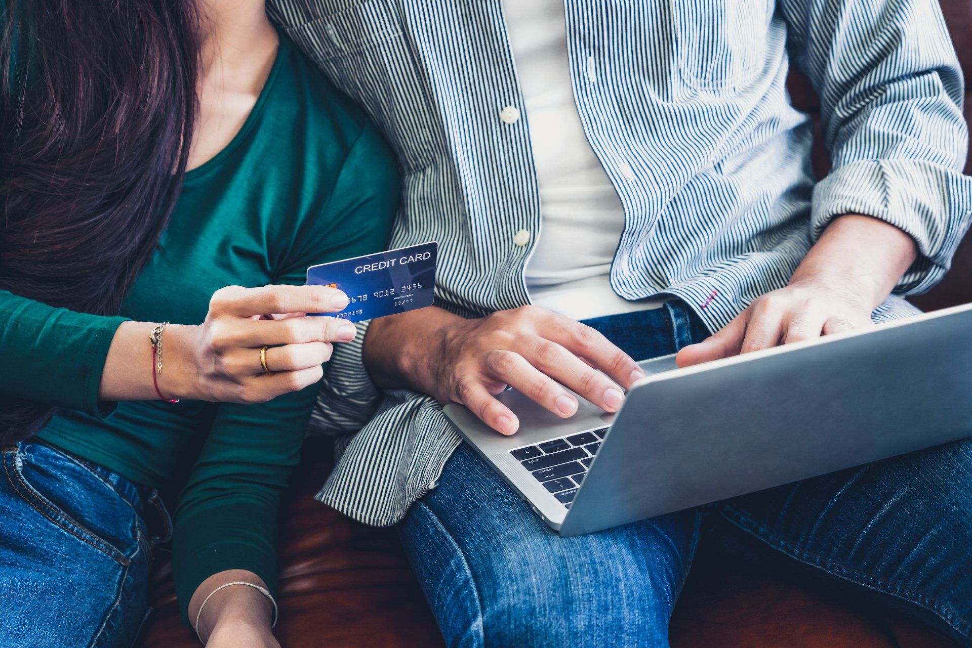 Two people on a couch using a laptop and holding a credit card