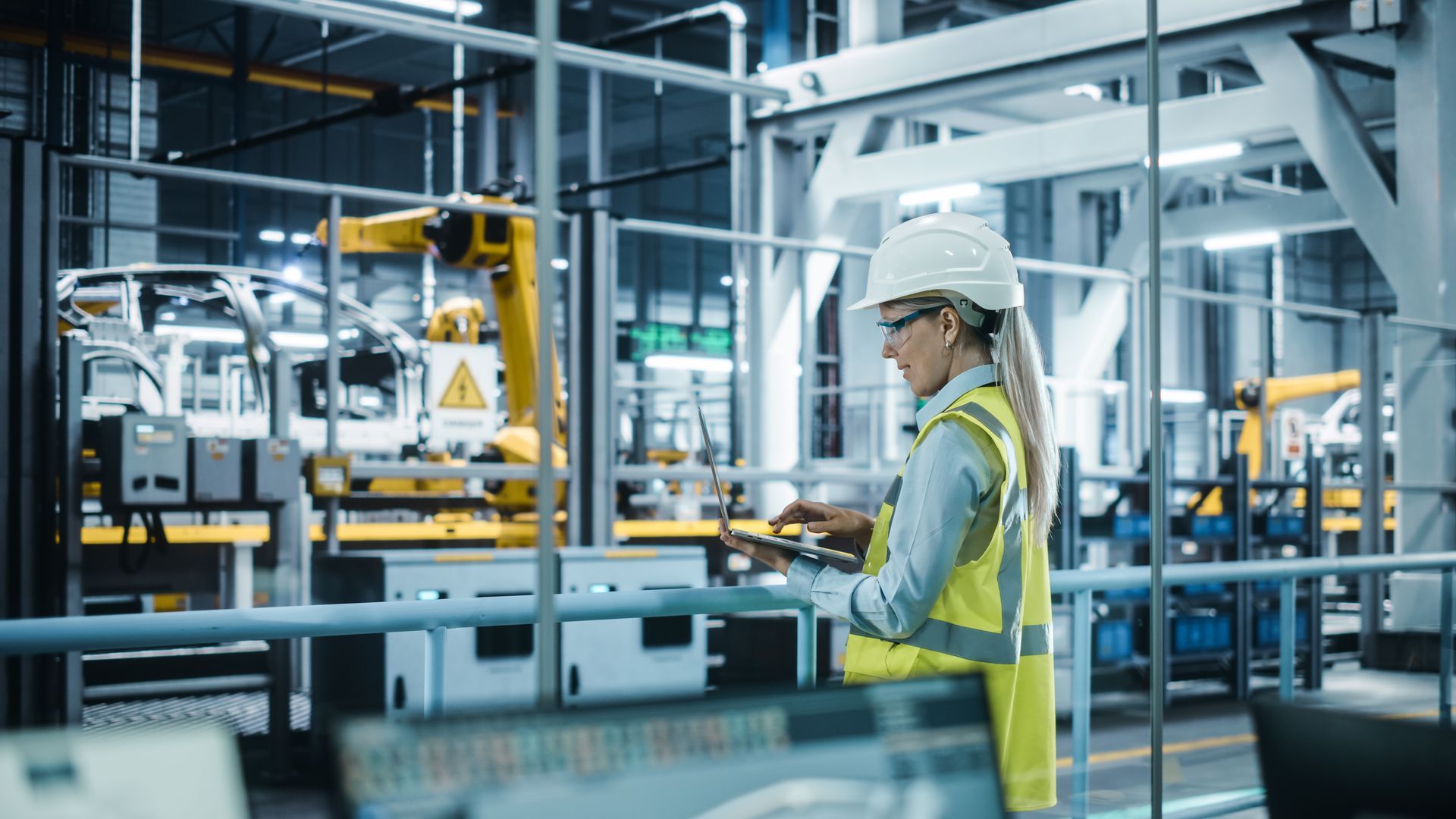 A woman is standing in a factory looking at a tablet.