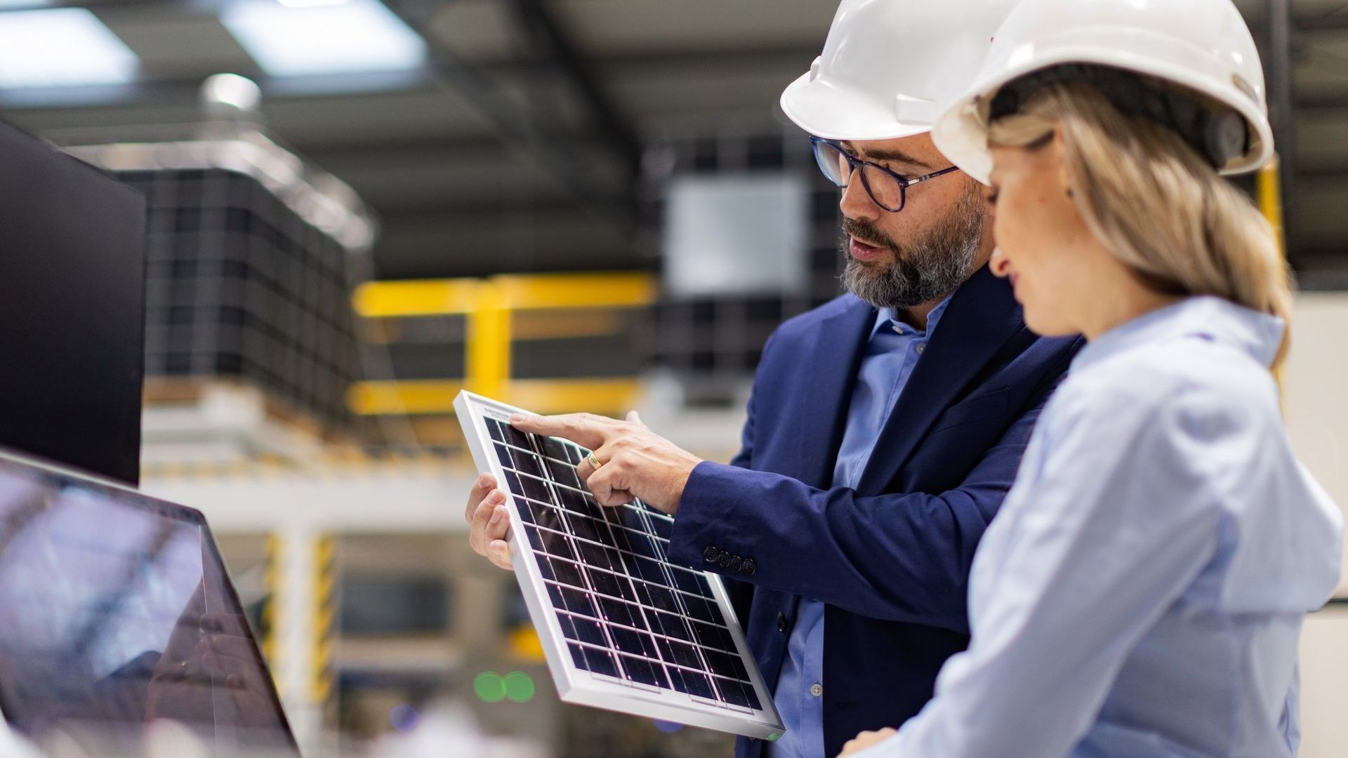 A man and a woman are looking at a laptop in a factory.