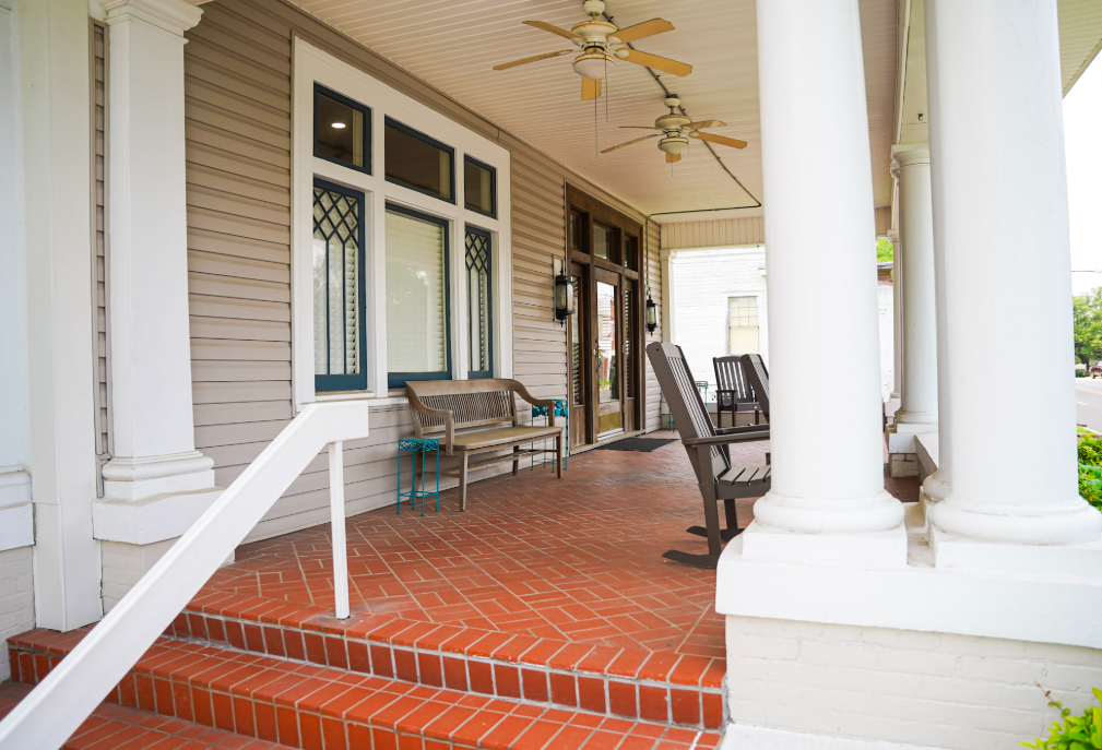 A porch with a bench and chairs and a ceiling fan.