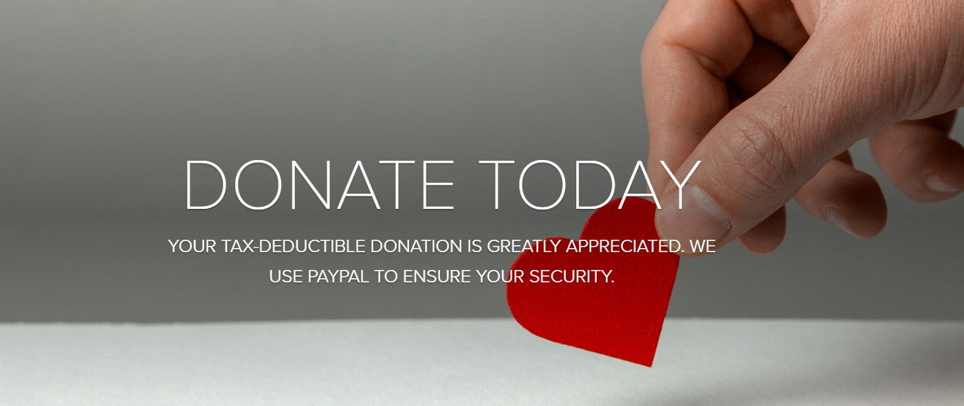 A hand is holding a red heart in front of a sign that says donate today