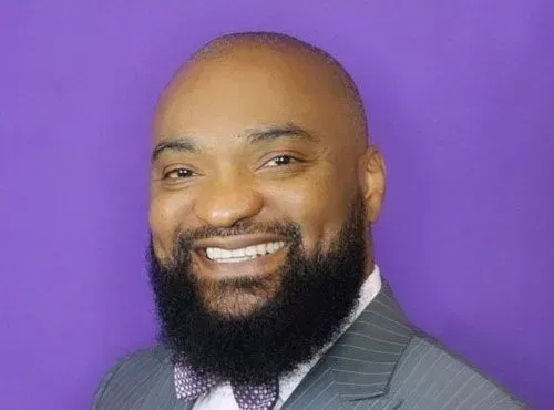 A man with a beard is wearing a suit and bow tie and smiling.