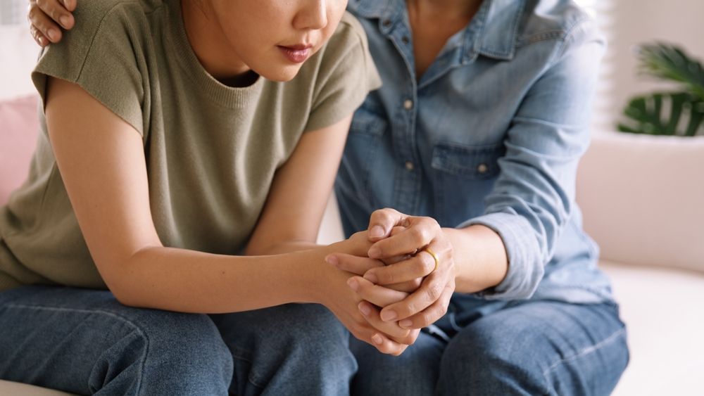 A woman is comforting a young girl while sitting on a couch.