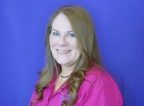 A woman in a pink shirt is smiling in front of a blue background.