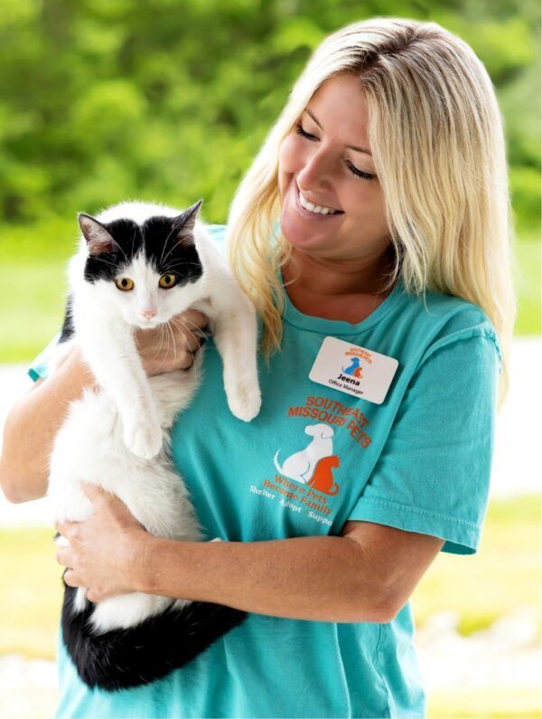 A woman in a blue shirt is holding a black and white cat