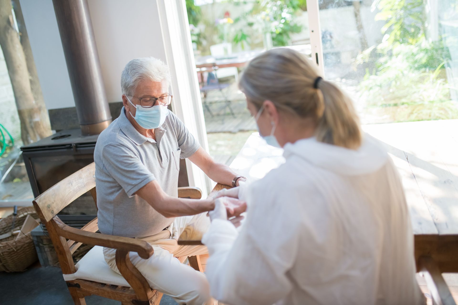 Masked patient and caregiver talking on a sunlit porch