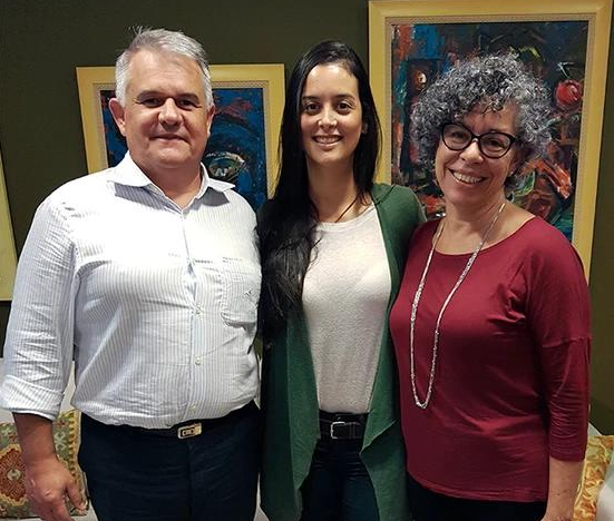 Um homem e duas mulheres posam para uma foto em frente a pinturas.