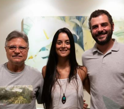 Dois homens e uma mulher posam para uma foto em frente a uma pintura
