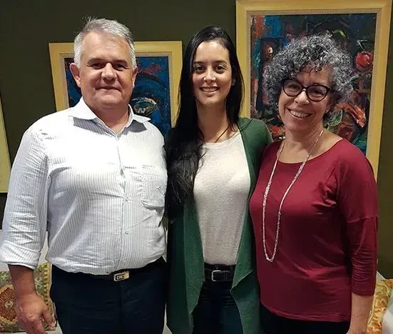 Um homem e duas mulheres posam para uma foto em frente a pinturas.