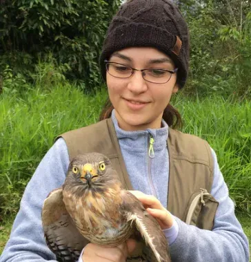 Uma mulher de óculos e gorro está segurando um pássaro