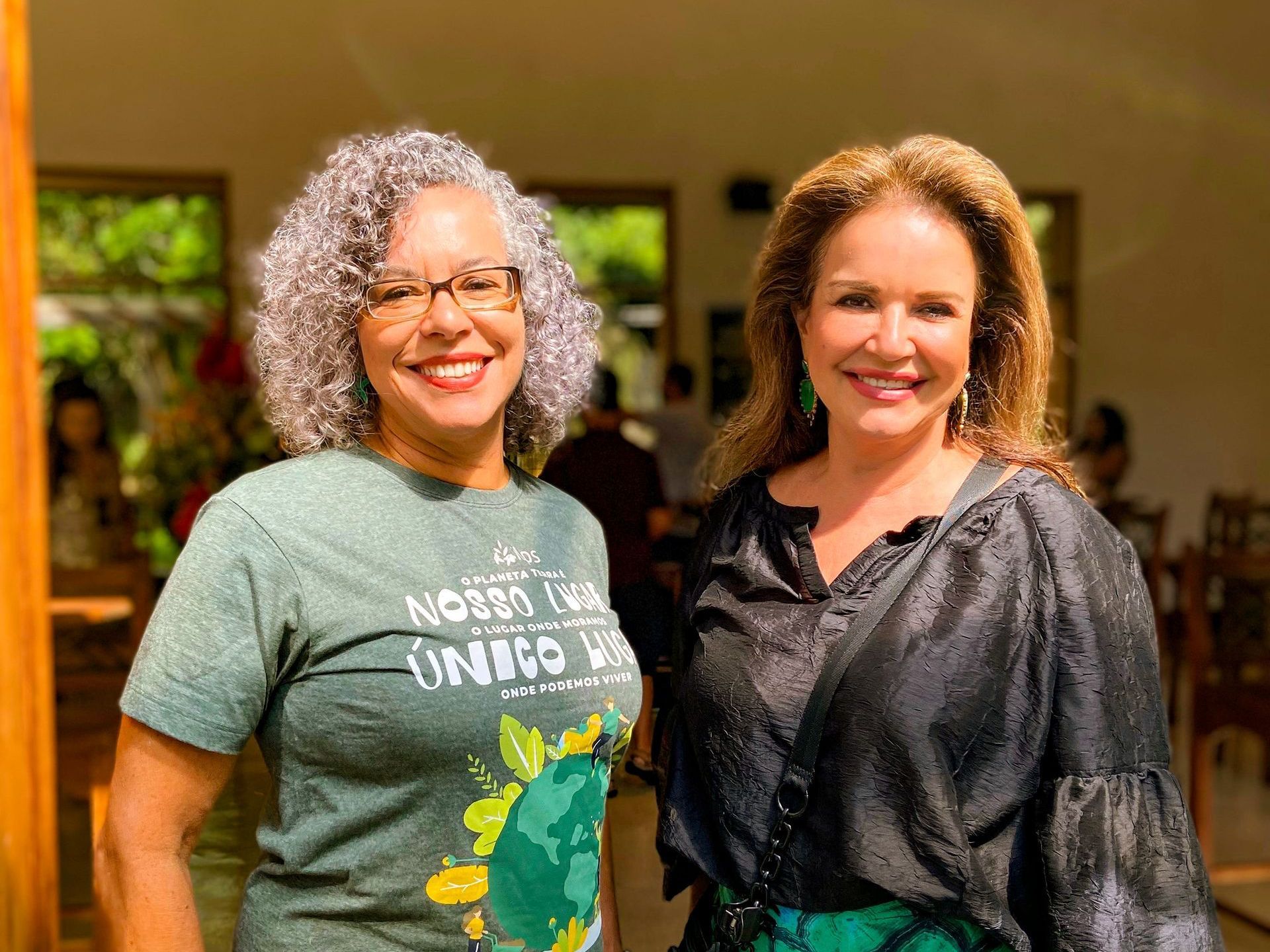 Duas mulheres estão próximas uma da outra e sorrindo para a câmera. uma das mulheres está vestindo uma camisa verde.