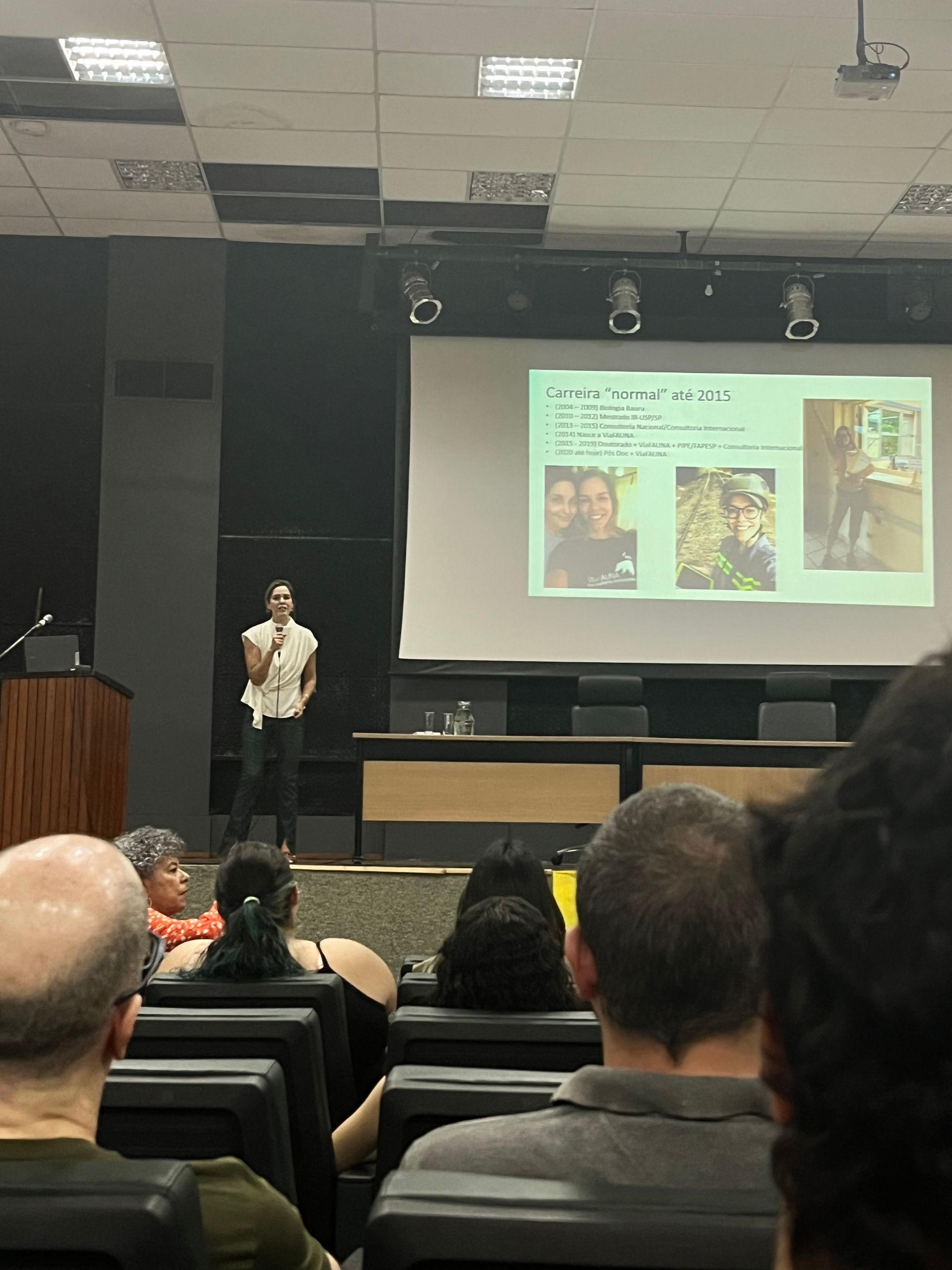 Uma pessoa apresentando uma apresentação de slides em uma sala de aula, com uma multidão de participantes sentados