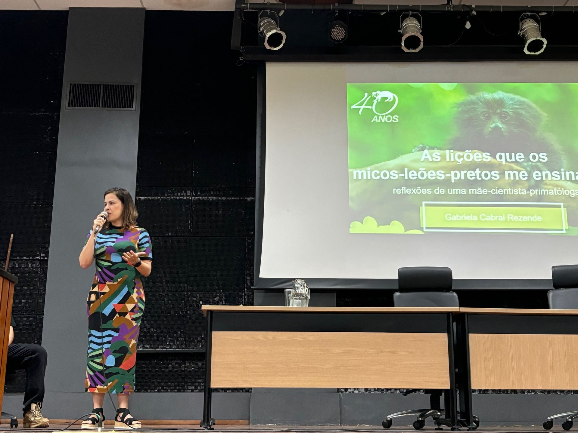 Mulher fazendo uma apresentação no palco, segurando um microfone.