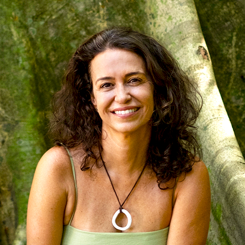 Uma mulher usando um colar com um pingente circular está sorrindo na frente de uma árvore