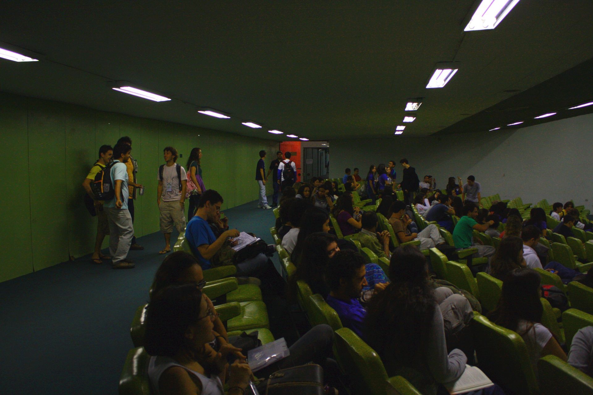Um grupo de pessoas está sentado em uma sala com cadeiras verdes.