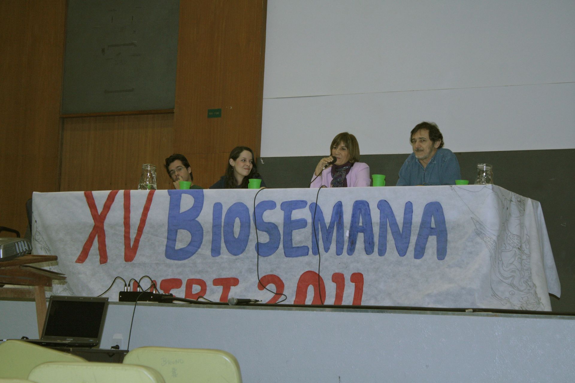 Três pessoas sentadas em uma mesa com uma placa que diz xv biosemana