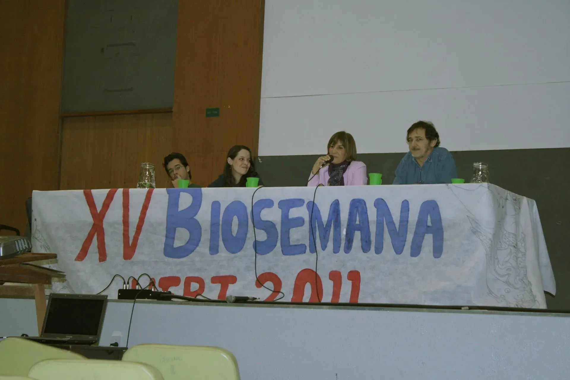 Três pessoas sentadas em uma mesa com uma placa que diz xv biosemana