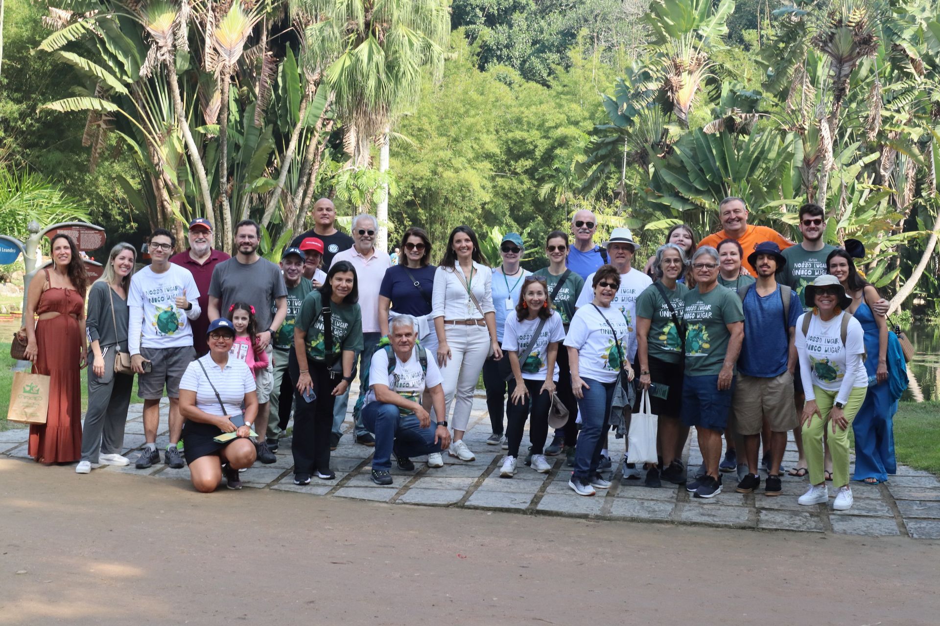 Grupo de pessoas sorrindo para uma foto ao ar livre, em um parque verdejante. 
