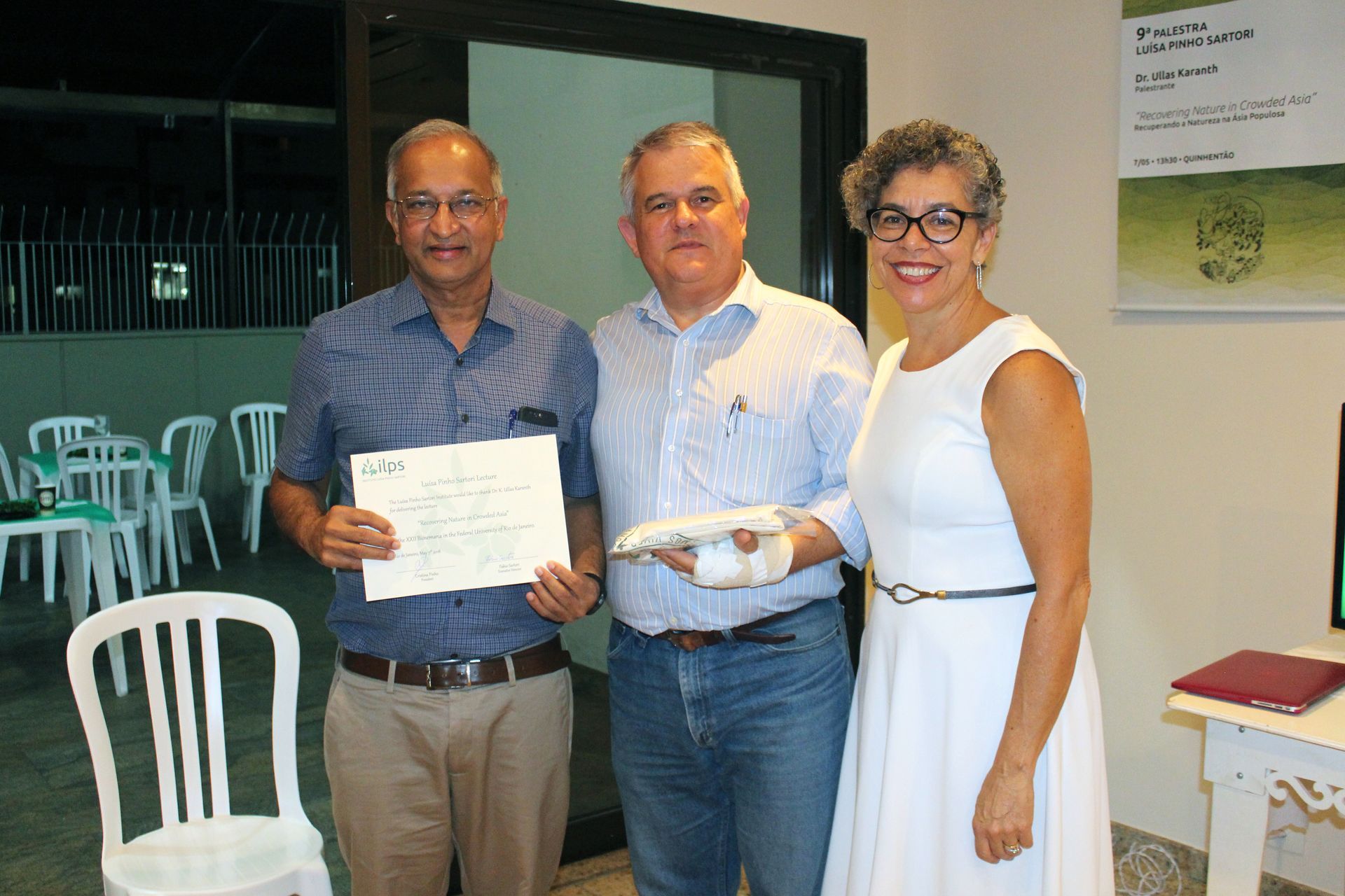 Três pessoas estão lado a lado em uma sala segurando um certificado.