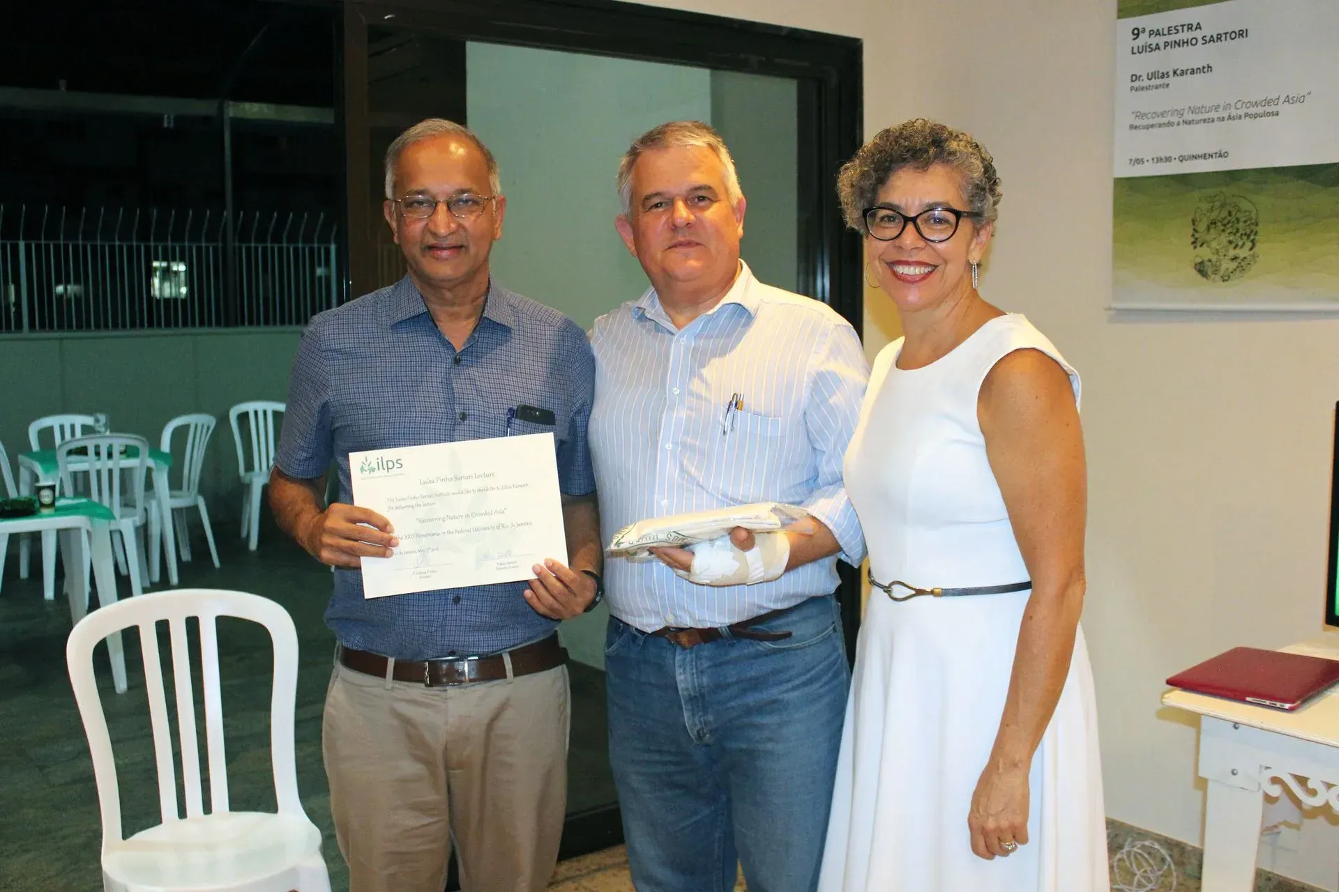 Três pessoas estão lado a lado em uma sala segurando um certificado.