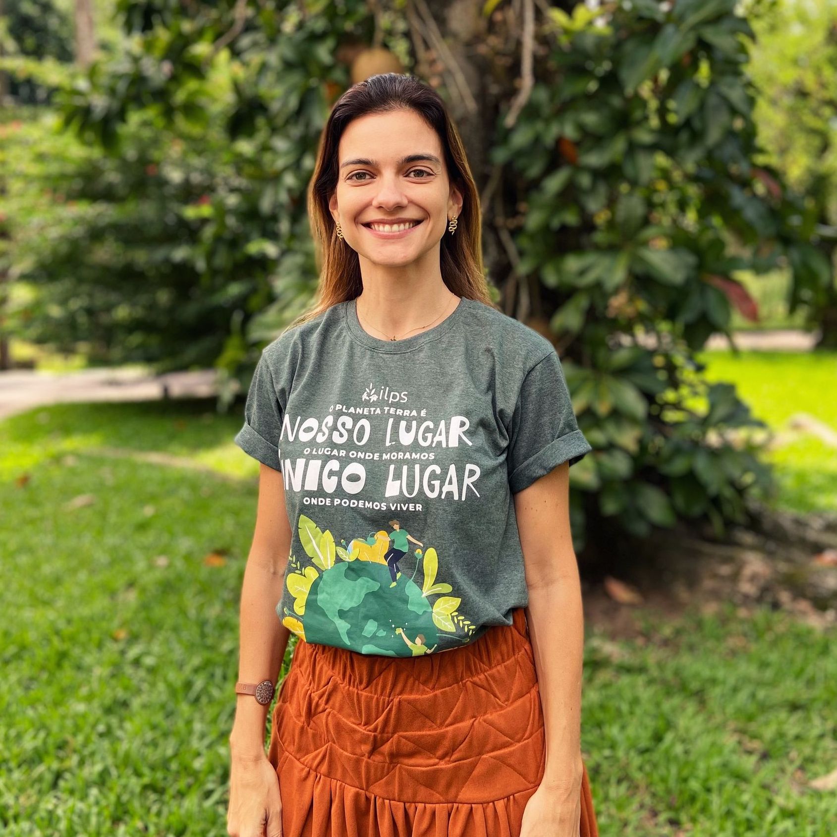 Uma mulher vestindo uma camiseta e uma saia está parada em um parque.