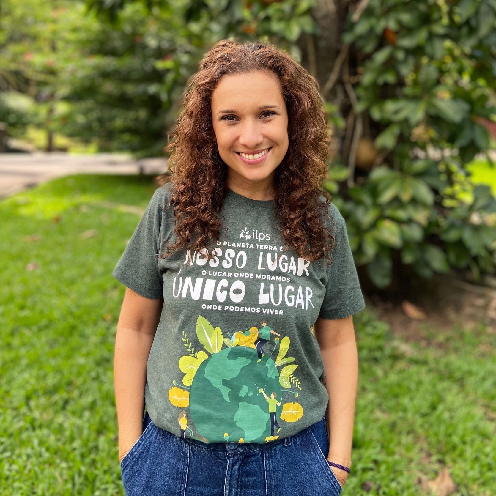 Uma mulher vestindo uma camiseta com a imagem de um globo está parada na grama.