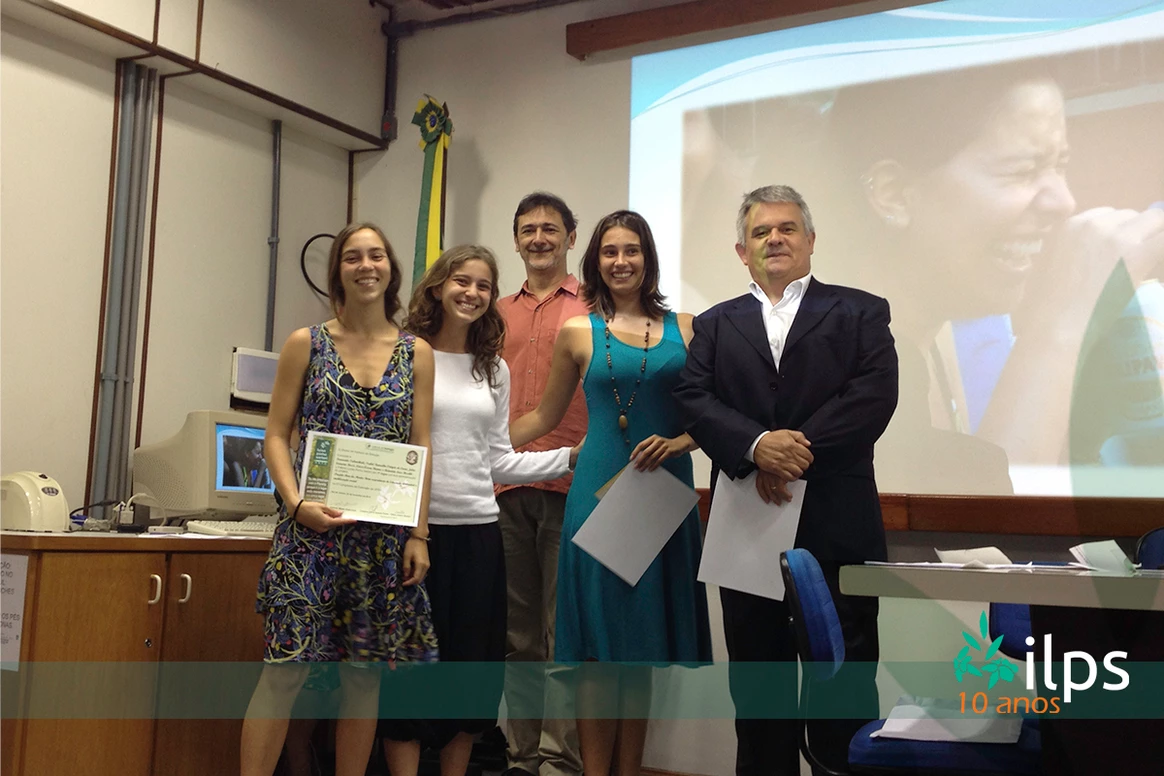 Um grupo de pessoas posa para uma foto em frente a uma tela de projetor que diz ilps