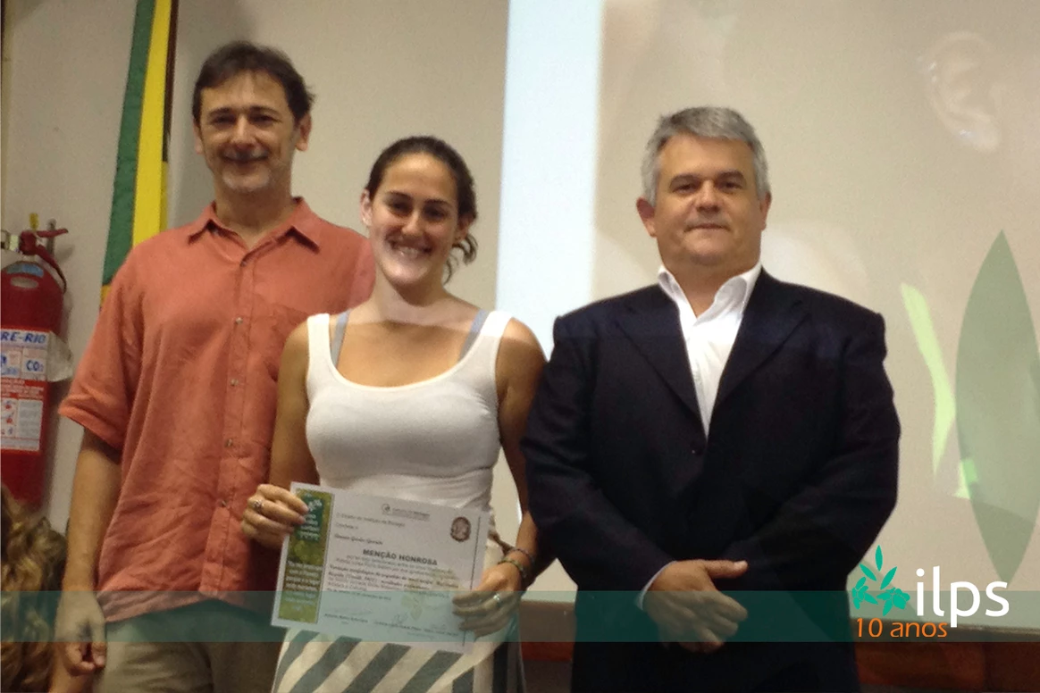 Uma mulher com um certificado fica entre dois homens e um extintor de incêndio