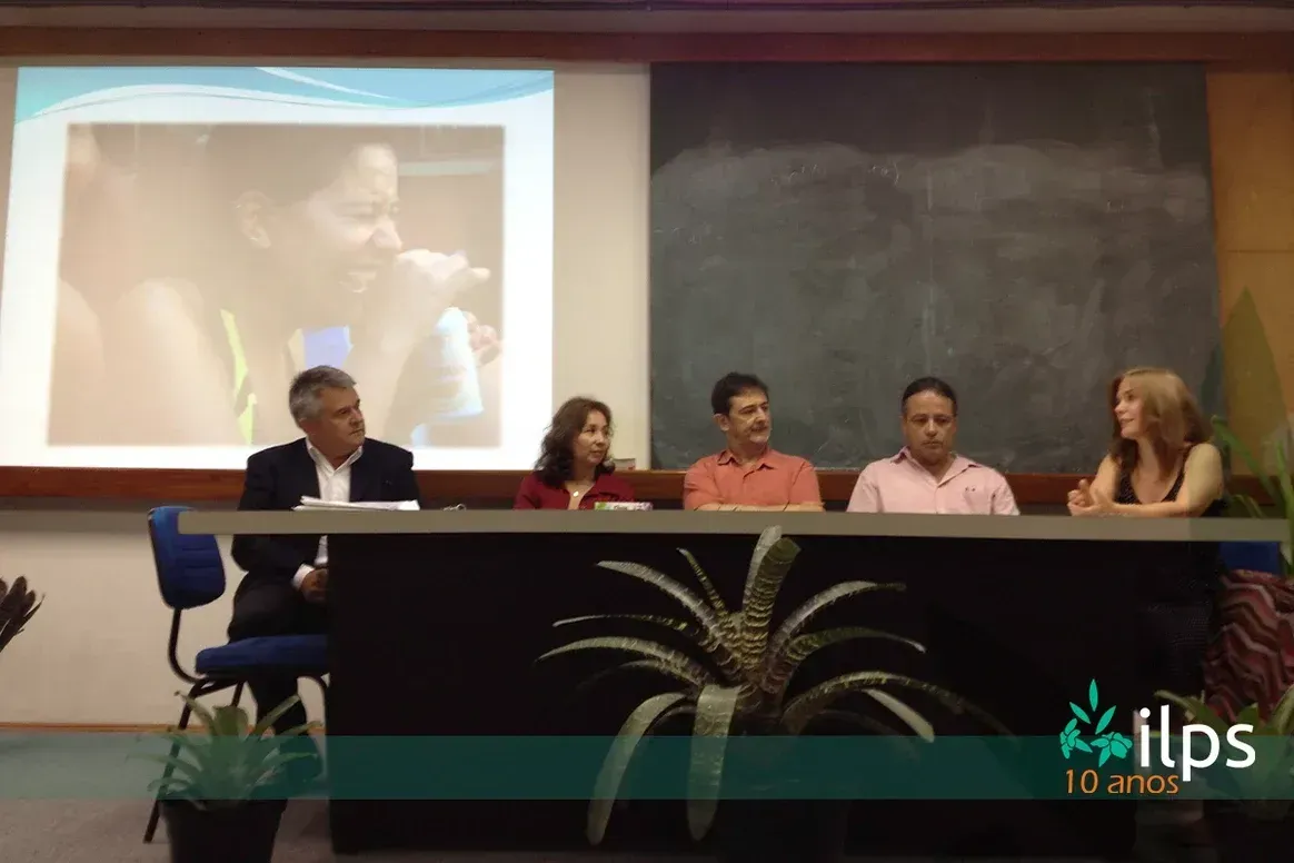 Um grupo de pessoas está sentado em uma mesa em frente a uma tela de projetor que diz itps