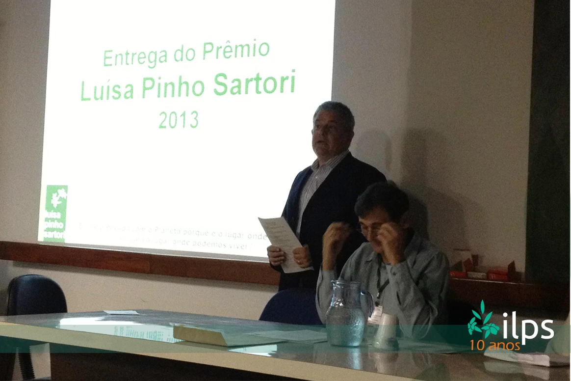 Um homem diante de uma tela que diz entrega do prêmio luisa pinho sartori 2013