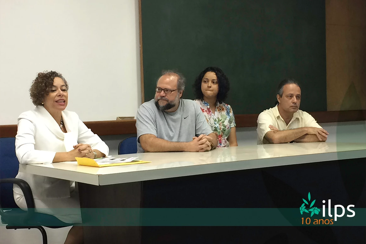 Um grupo de pessoas está sentado em uma mesa em frente a um quadro negro.