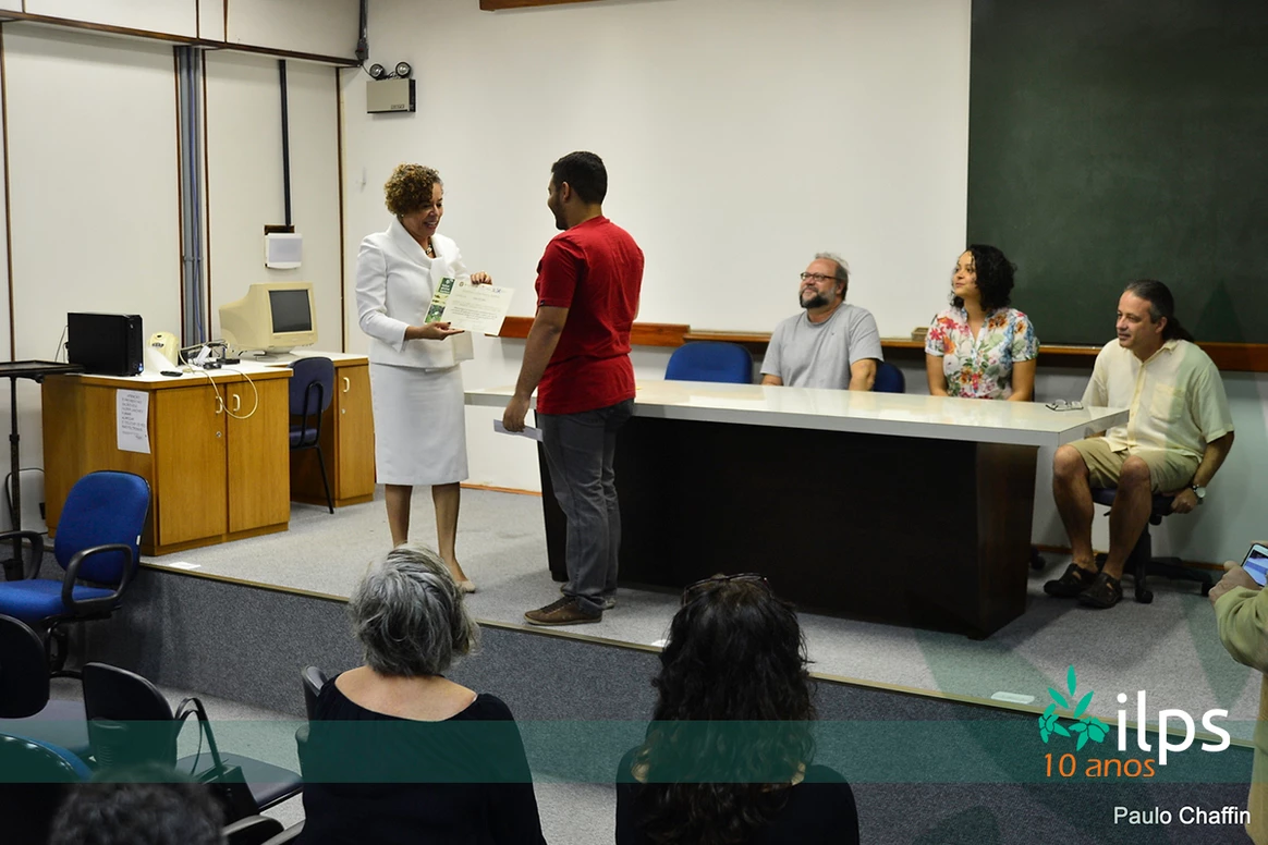 Uma mulher está dando um certificado a um homem na frente de um grupo de pessoas