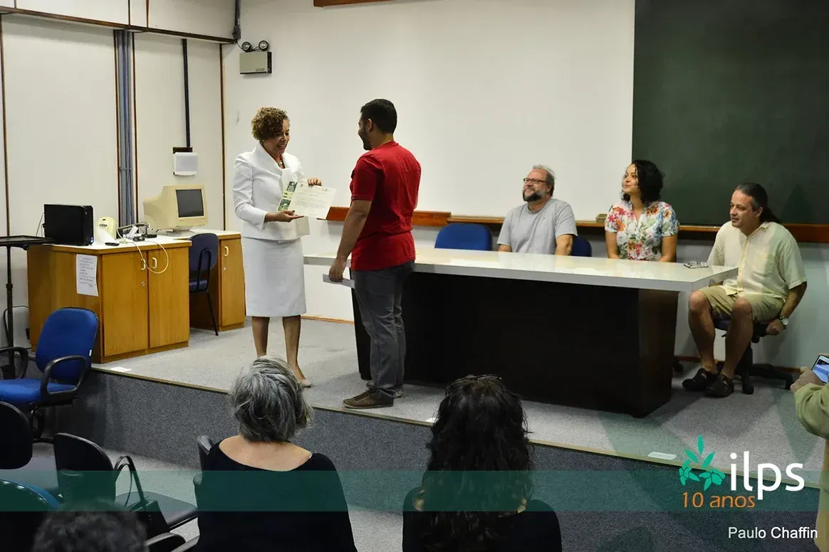 Uma mulher está dando um certificado a um homem na frente de um grupo de pessoas