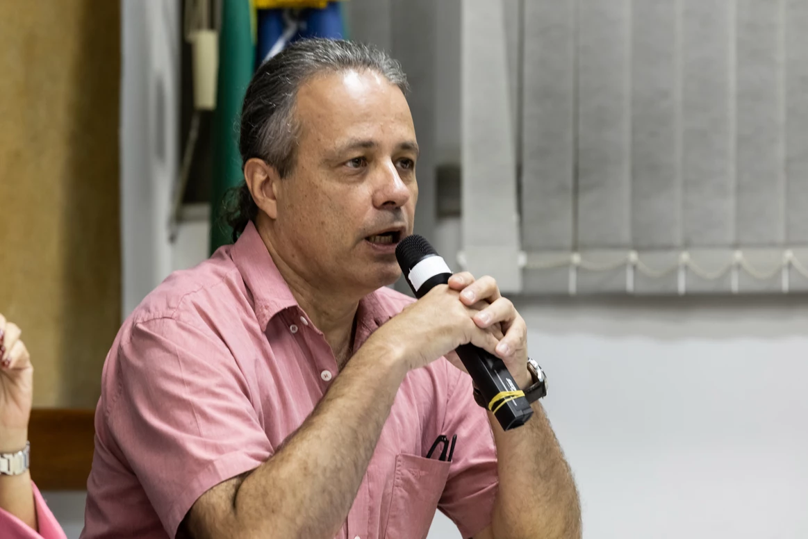 Um homem de camisa rosa está segurando um microfone na boca.