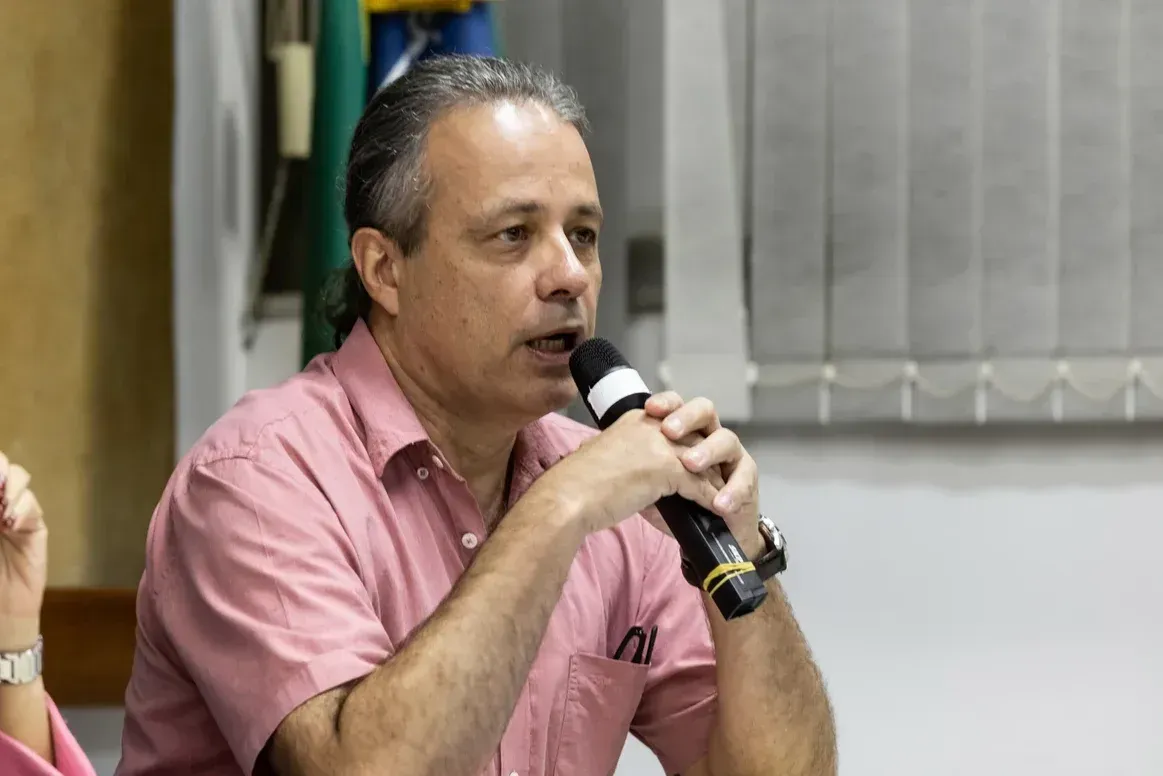 Um homem de camisa rosa está segurando um microfone na boca.