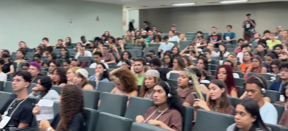 Um grande grupo de pessoas está sentado em uma sala de aula.