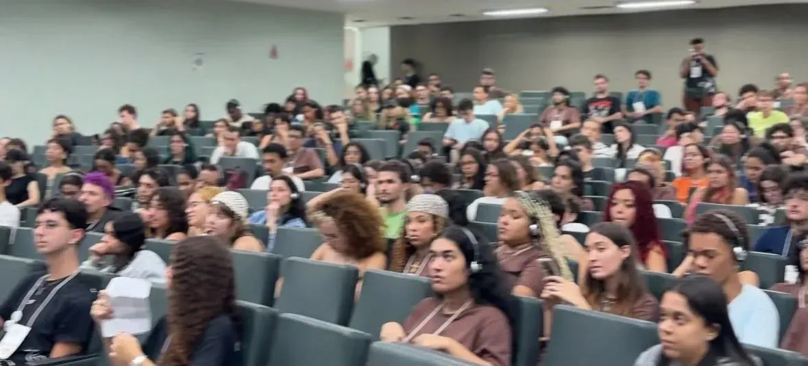 Um grande grupo de pessoas está sentado em uma sala de aula.